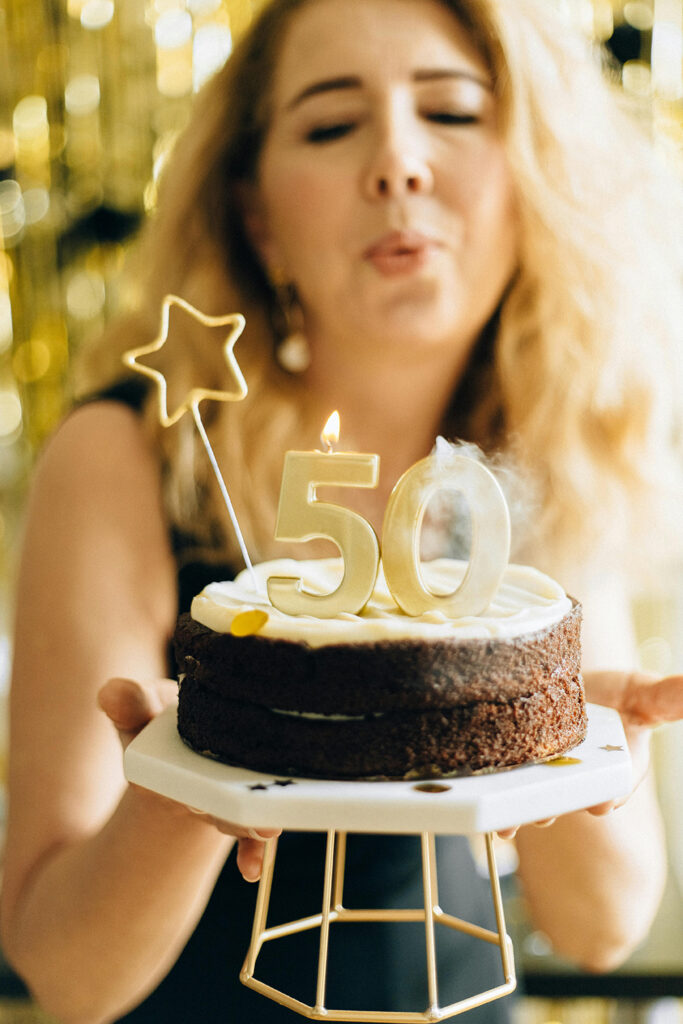 A 50 year old woman with menopause blowing out her birthday cake wishing for a holistic nauturopathic doctor